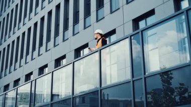 Modern bir binanın terasında cep telefonu kullanarak yürüyen kendine güvenen bir mimar.