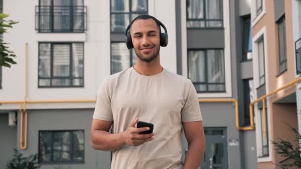 非洲裔美国年轻人 头戴黑色耳机 在街上用手机走路 听音乐 互联网 科技城市外的手机 — 图库视频影像