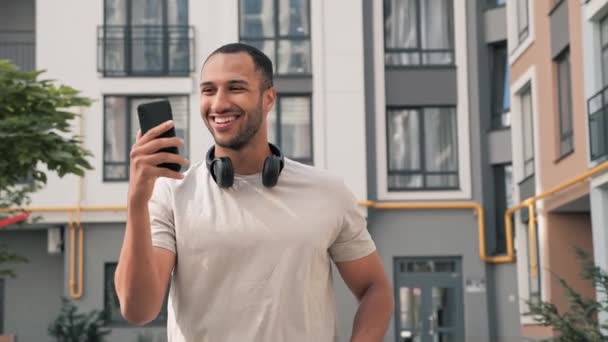 一个成功的笑着的非洲男人领头羊走在大街上 一边看手机 一边用智能手机在网上聊天 一边读好消息 这使得在户外开电话会议成为可能 — 图库视频影像