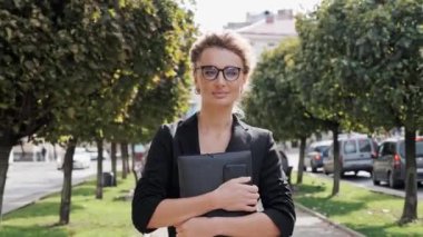 Kendine güveni tam bir iş kadını, elinde belgelerle şehir sokaklarında yürüyor, şık iş kıyafetleri ve gözlük takıyor. Dışarıdaki kameraya bakan genç sarışın kadın. Başarı. - Kadın. İnsanlar
