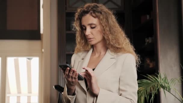 ホテルのロビーで携帯電話を探している集中ビジネス女性 オフィスラウンジでスマートフォンを使う女性 カフェで携帯電話でモバイルメッセージを読むスタイリッシュなビジネス女性の肖像画 — ストック動画