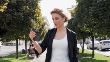 Güzel, mutlu, genç, mavi gözlü kıvırcık saçlı, şık elbiseli bir iş kadını. Bir video görüşmesi yapıyor. Gülerek konuşuyor.