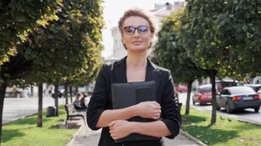 Resmi gözlüklü hoş bir iş kadını elinde belgelerle şehir caddesinde yürüyor. Kendine güvenen ve şık giyimli bir iş kadını sokakta yürüyor.
