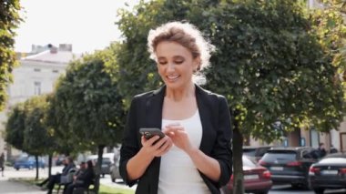 İş yerindeki başarısını kutlamak için elinde akıllı telefonla el kol hareketi yapan resmi kıyafetli neşeli beyaz iş kadını. Zafer, piyango, teknoloji insanları konsepti