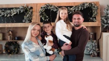 Aile fotoğrafı, Noel. Çocuklarıyla el ele tutuşup evdeki kameraya bakan güzel evli çift. Oğlan ve kızı yumuşak oyuncaklar tutuyorlar. Yeni yıl mutfağında güzel bir dekor.