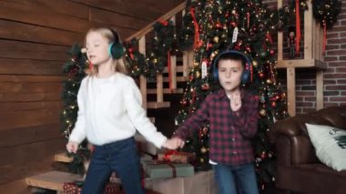 Kulaklıklı çocuklar müzik dinliyor, dans ediyor Noel Ağacı 'nın yanında eğleniyorlar. Küçük çocuklu mutlu bir aile Noel arifesini kutluyor. Şenlikli Noel ağacı evinde eğlenceli müzikler dinliyor.