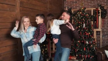 Ebeveynler çocuklarını ellerinin arasına alıp Noel Ağacı 'nın yanında dans ediyorlar. Parlayan Noel ağacı evinde Noel arifesini kutlarken mutlu aktif aile dansları. Yeni yıl kış tatili konsepti