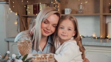 Süslü bir Noel mutfağında bir anne ve küçük güzel kızının büyüleyici portresi. Anne kızı kucaklıyor. Yeni yıl arifesi. Tatil hazırlığı. Parıltılı ışıklar. - Aile. Yakından bak.