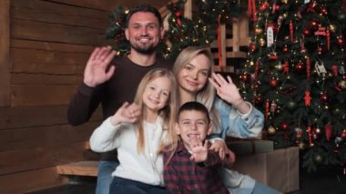 Mutlu neşeli aile, Noel ağacının yanında el sallayarak evde şenlikli kış tatilinin tadını çıkarıyor. Anne, baba, küçük oğlan ve kız kameraya bakıp selam verin. Yeni Yıl