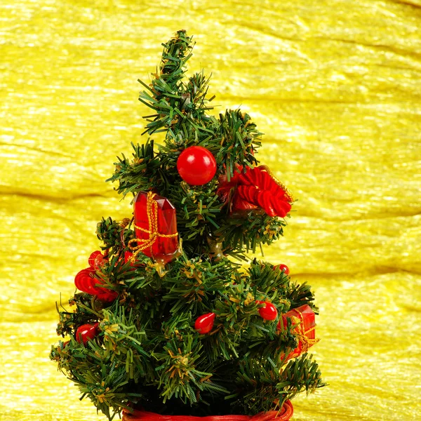 Kleiner geschmückter Weihnachtsbaum auf goldenem Hintergrund mit Geschenken — Stockfoto