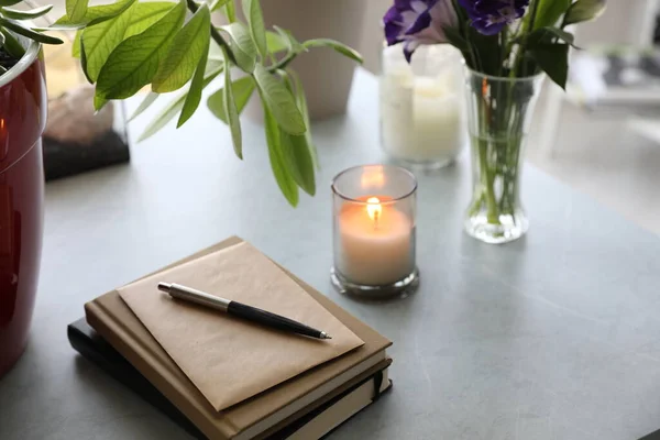 Defterler, çiçekler ve masada bir mum.