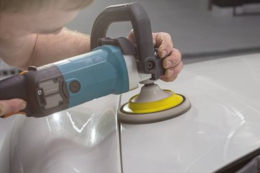 Araba temizliği ve cilalama konsepti. Profesyonel araba servisi işçisinin elleri, yörünge cilasıyla, oto tamirhanesinde beyaz lüks araba kaputunu parlatıyor..