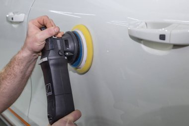 Bir araba servisi çalışanı araba vücudunu cilalama makinesiyle cilalıyor. Arabanın detaylandırılması ve parlatılması.