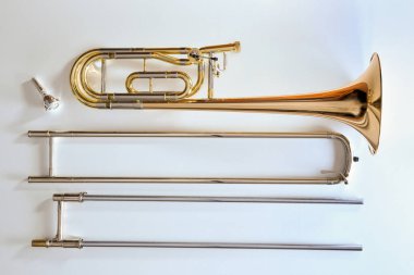 Trombon ve transpozör beyaz bir masa üzerinde parçalanmış. Üst Manzara. Yatay bileşim.