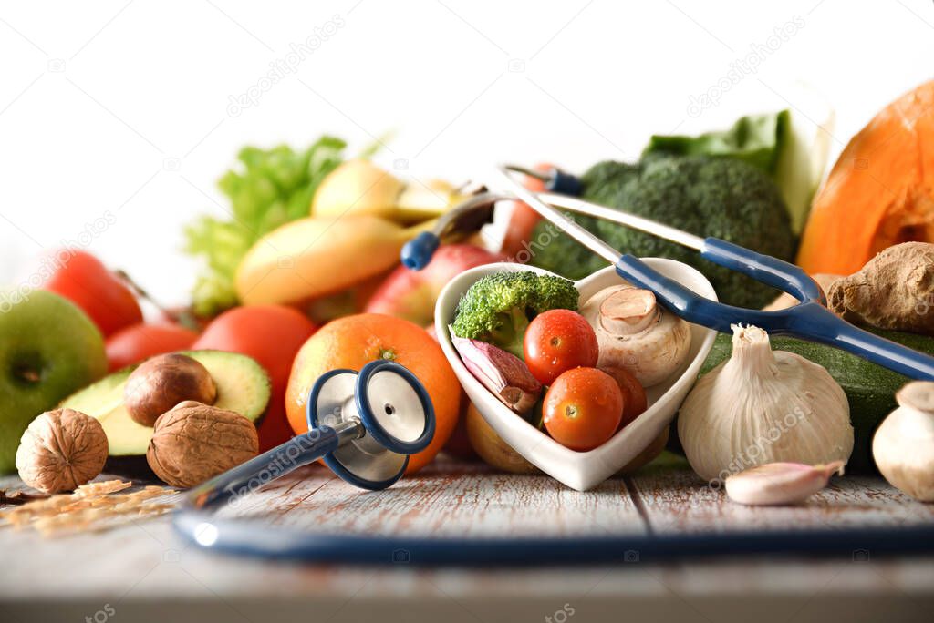 Healthy food concept with fruits and vegetables and stethoscope on wooden table. Front view. Horizontal composition.