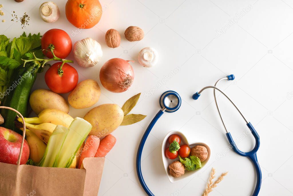 Shopping basket with healthy products on white table with stethoscope