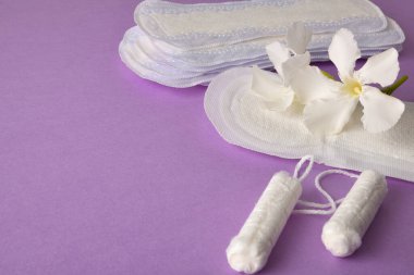 Korunma amaçlı bir grup ürün ve tampon, pamuk pedli adet hijyeni, tasarruf fişi ve leylak arka planda beyaz çiçek. Yüksek görünüm.