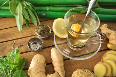 Bir fincan yeşil çay, üzerinde zencefilli nane ve ahşap masa üzerinde limon yaprakları, metal çaydanlık ve ahşap masa üzerinde bambu bastonlar. Yüksek görünüm.