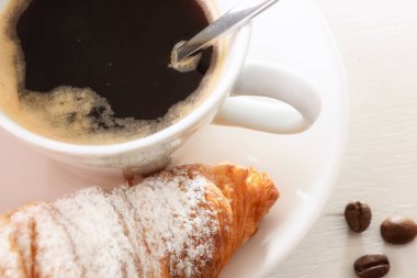 Kahvaltıda porselen beyaz fincanda sıcak kahve ve beyaz tabakta tatlı kruvasan. Üst Manzara. Yatay bileşim.