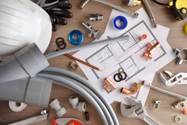 Material and tools for the installation of water in a house with a plan on a wooden workbench. Top view. Horizontal composition.