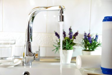 Open kitchen sink faucet flowing stream of water purified by domestic reverse osmosis with filters around. Front view. Horizontal composition.