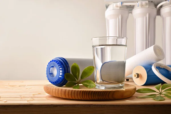 Glass of purified water with domestic equipment and environmentally friendly filters on wooden table isolated background with osmotizer equipment. Front view. Horizontal composition.