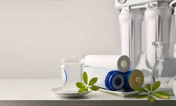 Glass and jug with purified water and domestic equipment with filters on white kitchen table and white isolated background. Front view. Horizontal composition.