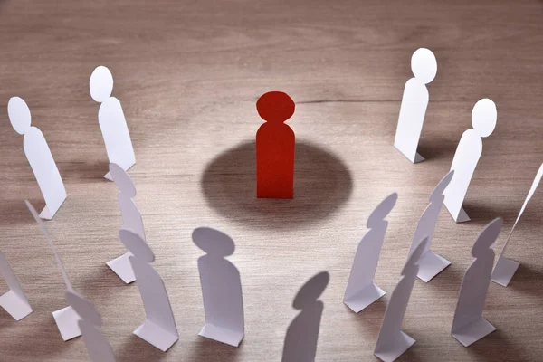 social discrimination concept with many little white paper men around a different one on wooden base and dark background front view