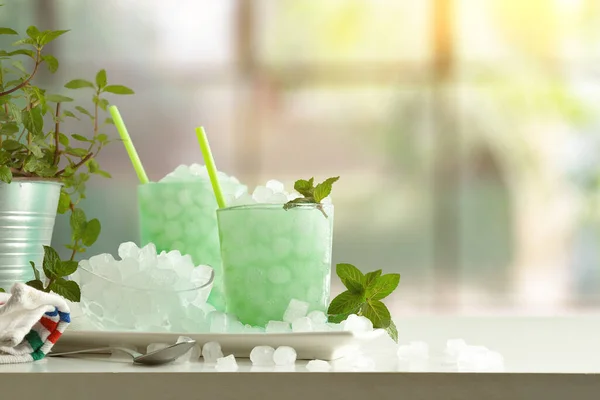Mint drink with a lot of ice on white table with plant and a window in the background. Front view. Horizontal composition.