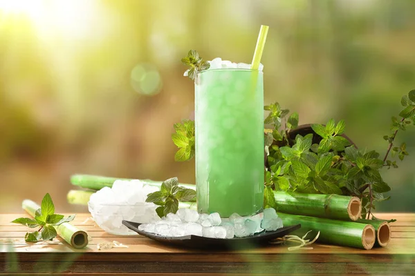Glass with natural mint drink with a lot of ice and mint leaves on a wooden table in the woods. Front view. Horizontal composition.