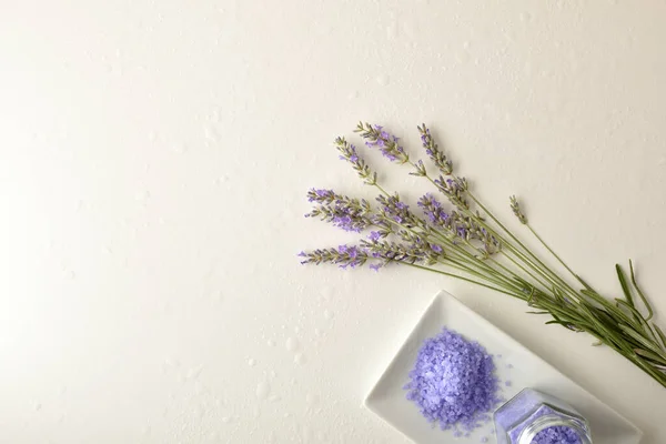 Background with lavender bath salts and bouquet of lavender spikes with flowers on white table with water drops. Top view. Horizontal composition.