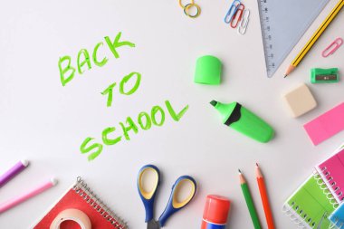 Background with the message back to school written with a green marker on a white desk and school supplies around it. Top view.