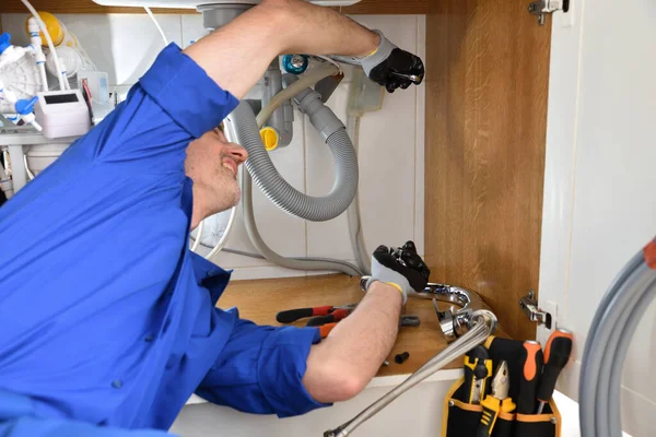 Detail of plumber in uniform repairing a leak under the sink in a home with tools around. Horizontal composition.