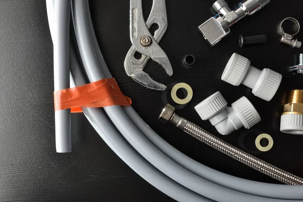 Detail of group of plumbing materials and tools on black table. Top view. Horizontal composition.