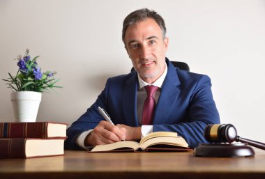 Ofis masasına kitap ve yargıç tokmağı ve izole beyaz duvar arkaplanıyla iyi bir avukat imzalıyor. Ön görünüm.