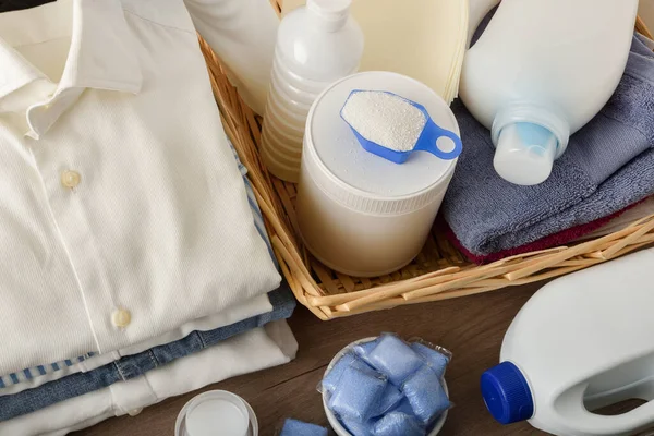 Detail of different types of laundry detergents on wooden table with freshly washed folded white clothes. Top elevated view. Horizontal composition.