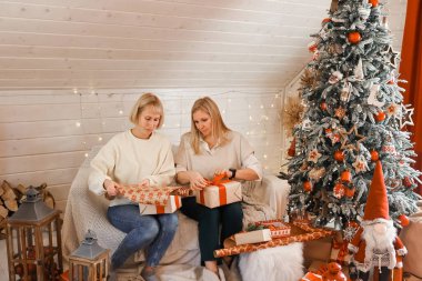 Mutlu kadın anneler Noel için hazırlanıyor, yeni yıl hediyeleri evde Noel ağacının yanında otururken paketleniyor. Kış tatili, ev dekorasyonu konsepti