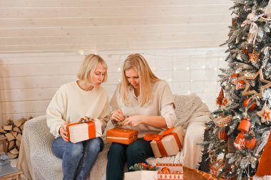 Mutlu kadın anneler Noel için hazırlanıyor, yeni yıl hediyeleri evde Noel ağacının yanında otururken paketleniyor. Kış tatili, ev dekorasyonu konsepti
