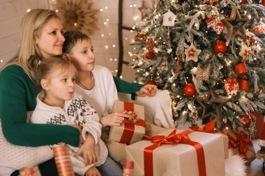 Morher ve Çocuklar yılbaşı atmosferinde. Aile Noel ve hediyelerle mutlu. Çocuklar yılbaşı ağacında hediyelerle.