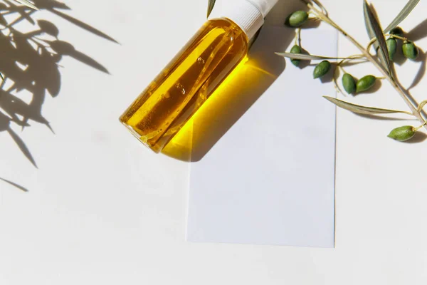 Green olive branch, olive oil and white empty paper card on white table background. Mockup, top view, flat lay.