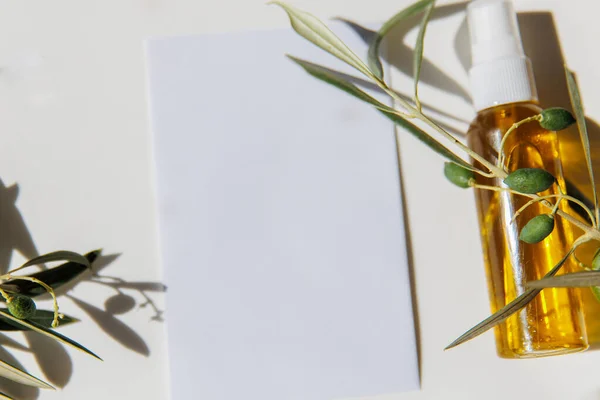 Green olive branch, olive oil and white empty paper card on white table background. Mockup, top view, flat lay.