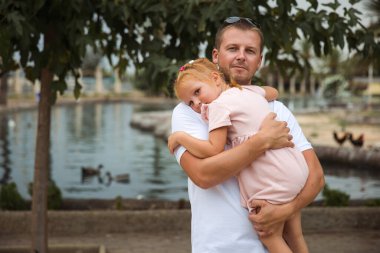 Dad holds his daughter in his arms, a walk in the city park, family leisure