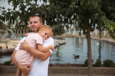 Dad holds his daughter in his arms, a walk in the city park, family leisure