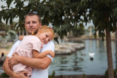 Dad holds his daughter in his arms, a walk in the city park, family leisure