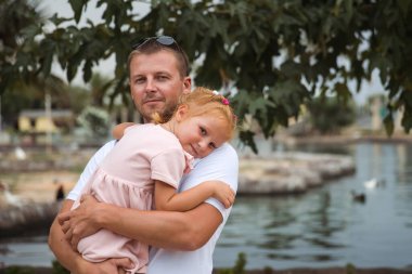 Dad holds his daughter in his arms, a walk in the city park, family leisure