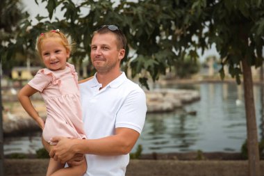 Dad holds his daughter in his arms, a walk in the city park, family leisure