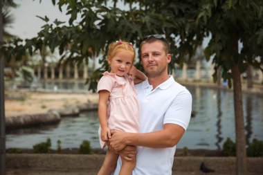 Dad holds his daughter in his arms, a walk in the city park, family leisure