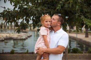 Dad holds his daughter in his arms, a walk in the city park, family leisure