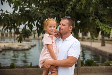 Dad holds his daughter in his arms, a walk in the city park, family leisure