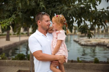 Dad holds his daughter in his arms, a walk in the city park, family leisure